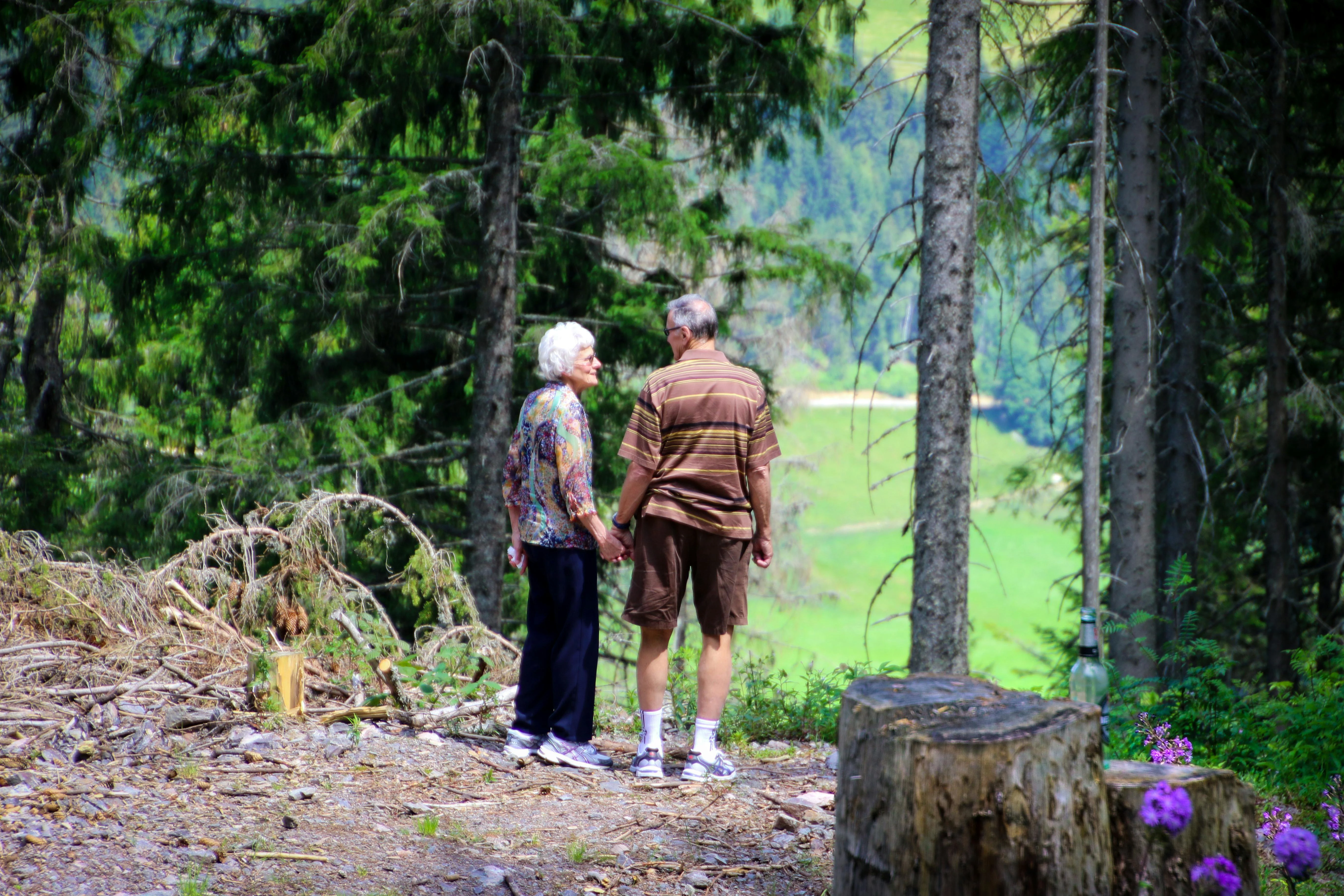 Un couple de personnes âgées, chaussées de chaussures du Foot Care Center by Spronken Orthopedie en Belgique, se promenant dans la forêt