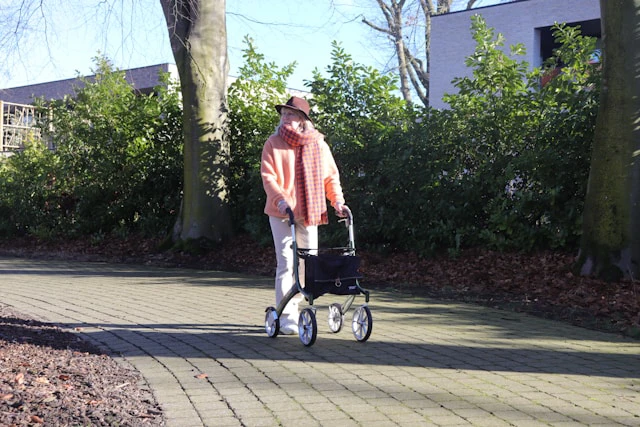 Une femme équipée d'un déambulateur se promène dans le parc avec des semelles sur mesure du Foot Care Center by Spronken Orthopedie