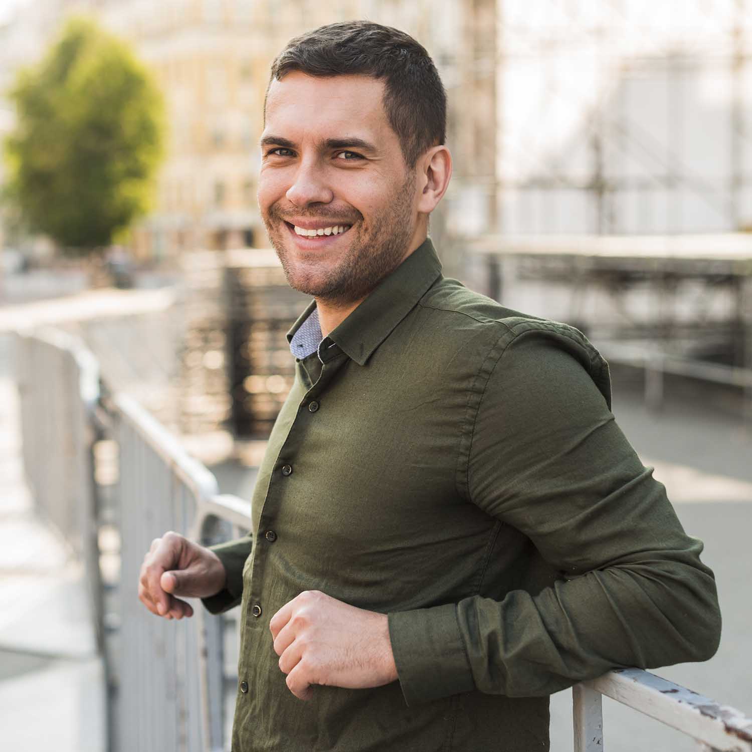 Happy Young Man Standing Near Metallic Railing Looking Camera