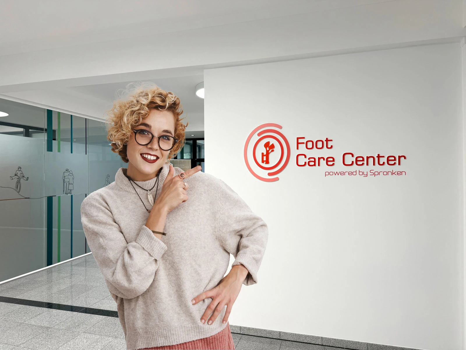 Une employée souriante de Spronken Orthopedie montre du doigt le logo du Foot Care Center sur le mur